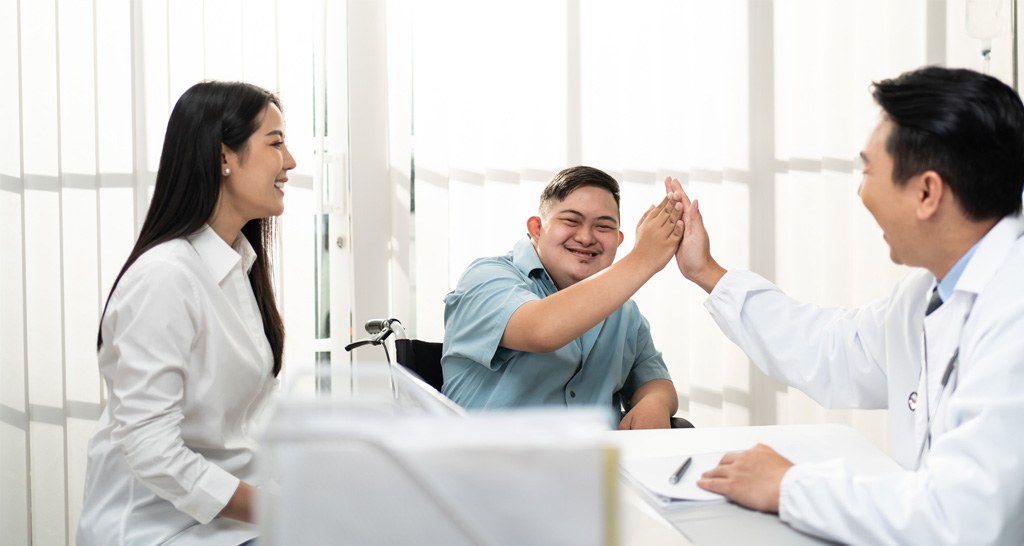 A handicap young man meeting with a male and a female healthcare working and giving a high five to the male doctor.