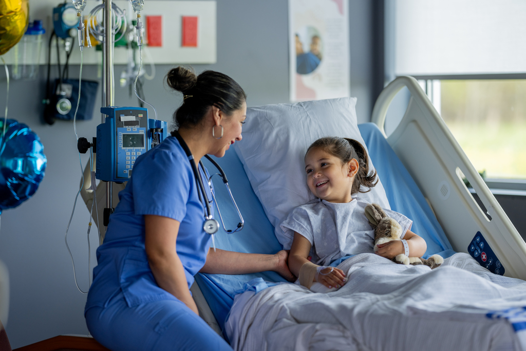A pediatrician comforts a child in a hospital bed